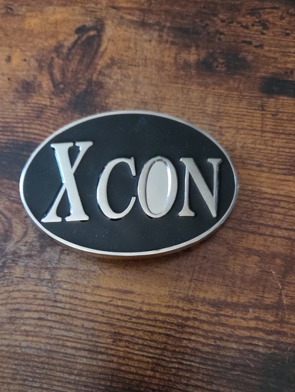 X-Con belt buckle featuring raised silver-tone lettering that reads "XCON"